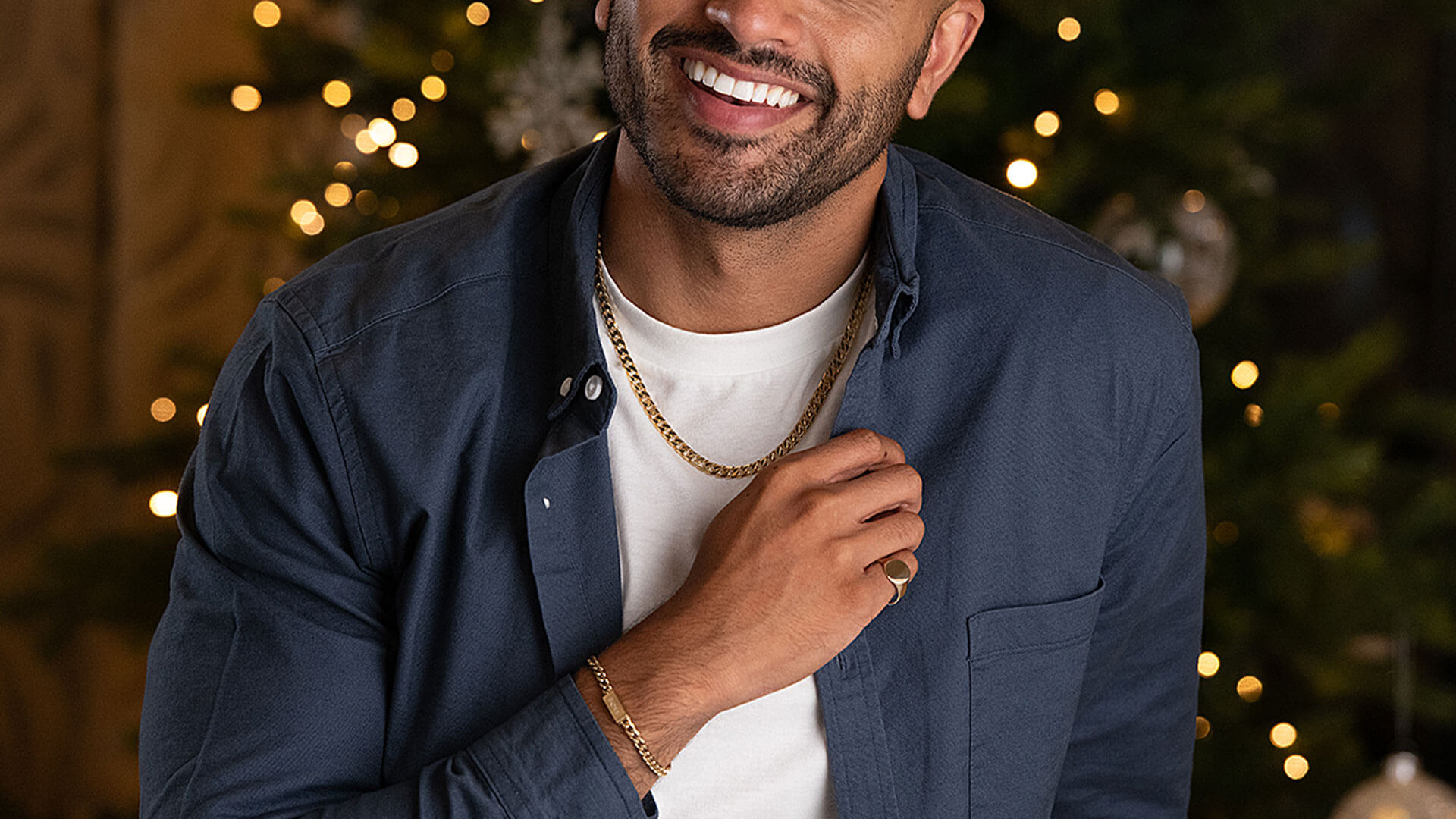  Smiling male model wears yellow gold plated curb chain and a 9ct gold oval signet ring by Beaverbrooks