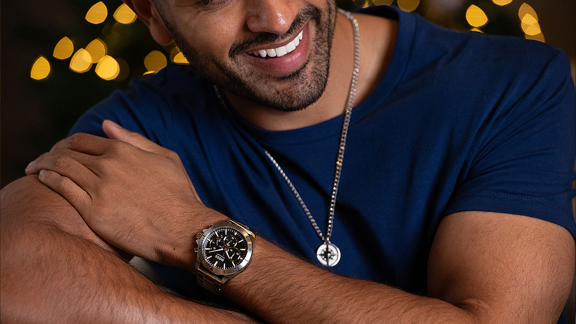 A smiling male model wears a silver pendant and a limited edition Troper watch, both by BOSS