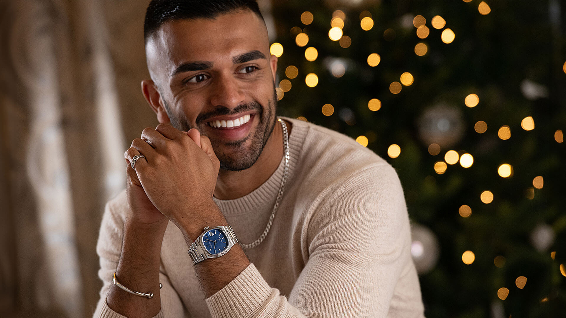 A smiling dark haired male model wearing silver party jewellery pieces and watch from Beaverbrooks