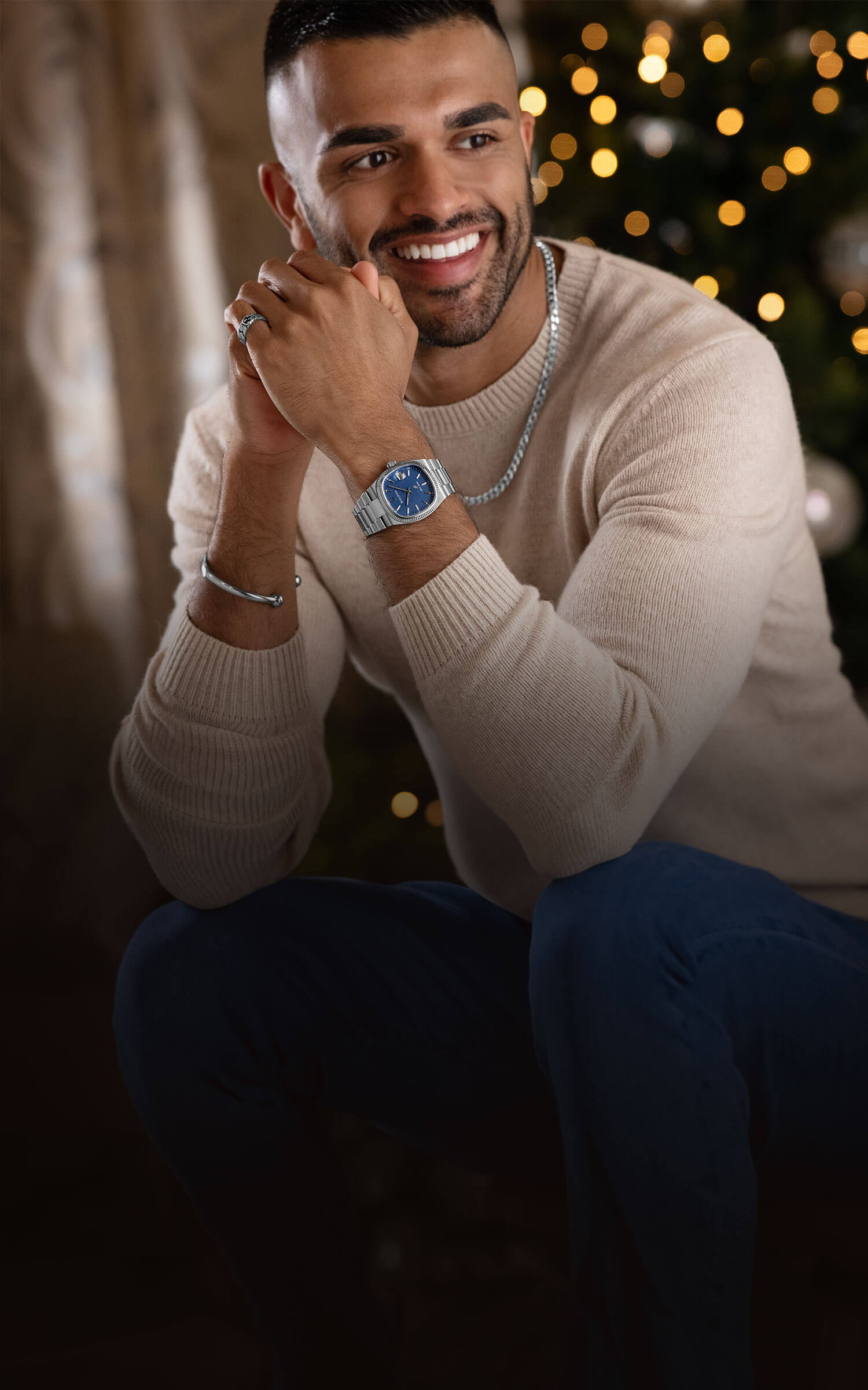 A smiling dark haired male model wearing silver party jewellery pieces and watch from Beaverbrooks